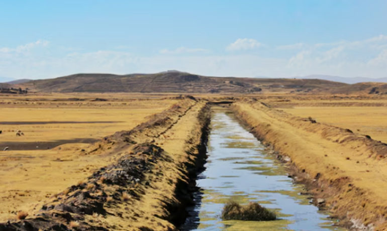 Irrigation canal cutting through desert terrain with hills in the background.
