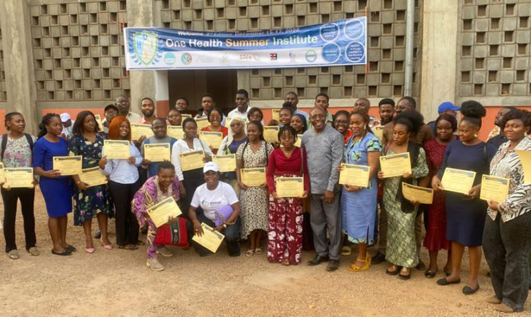Un grand groupe de participants et de mentors d’origines diverses se tient ensemble à l’extérieur, devant une bannière de la 3ᵉ édition de l’Institut d’été One Health, dont beaucoup tiennent des attestations papier.